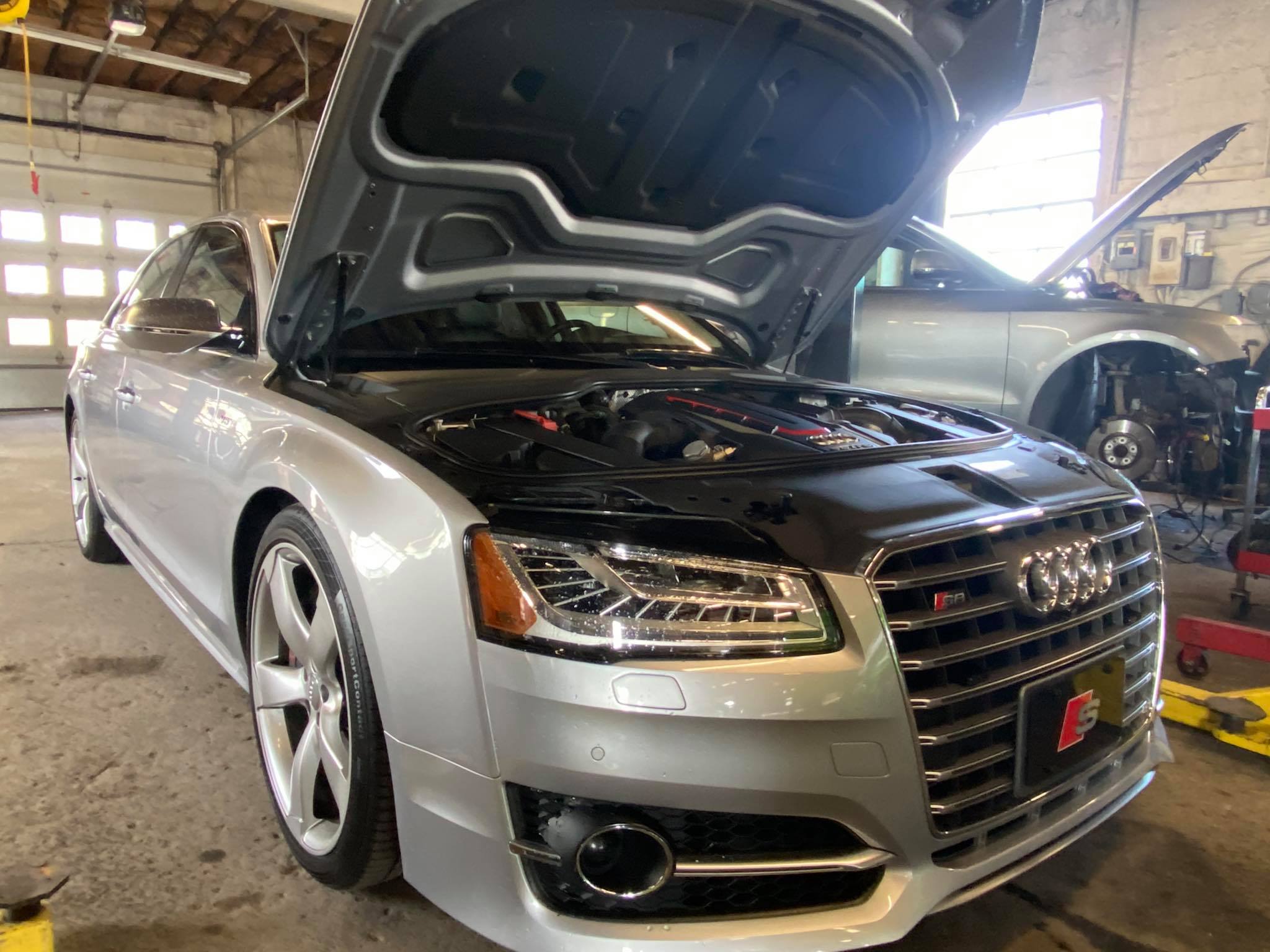 Silver Audi with hood open showing clean engine bay at European auto repair shop
